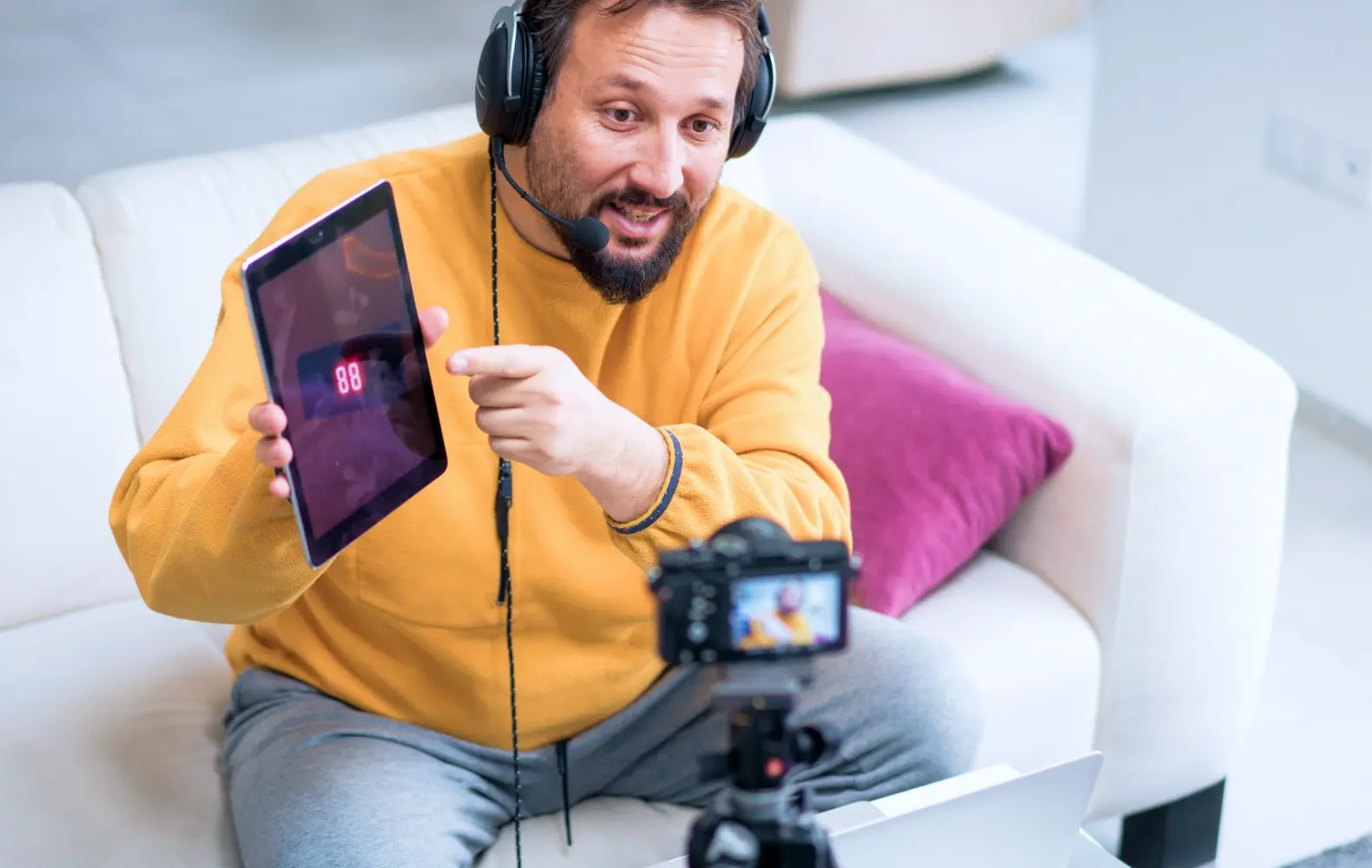 man in yellow sweatshirt with iPad in front of camera