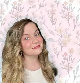 A young woman in a white top smiles in front of a floral patterned background