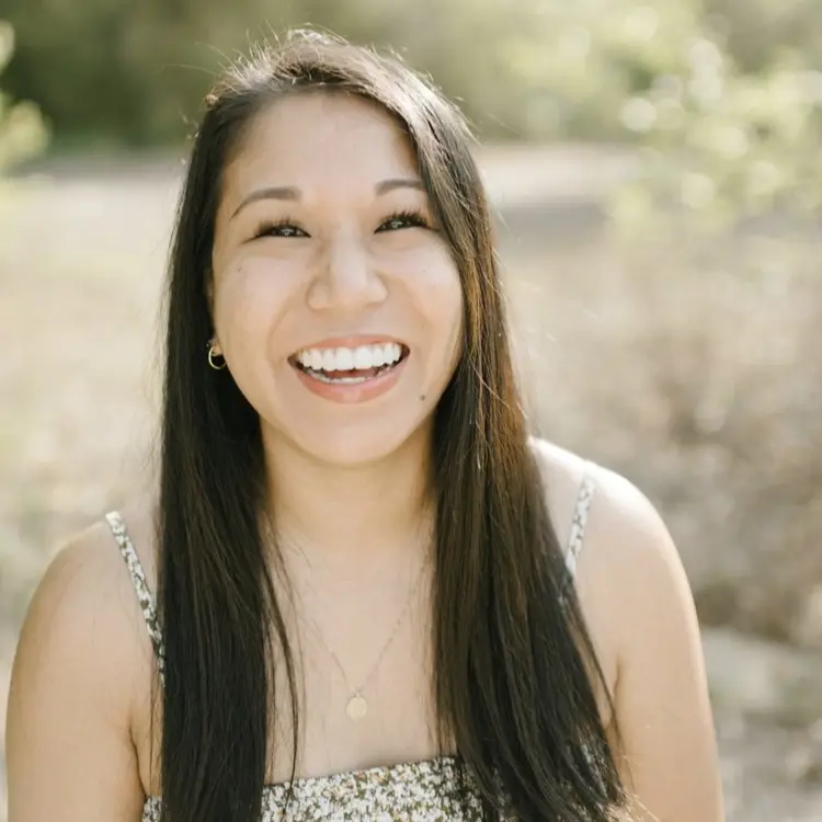 A woman with brown hair smiling at the camera, wearing a floral top. 