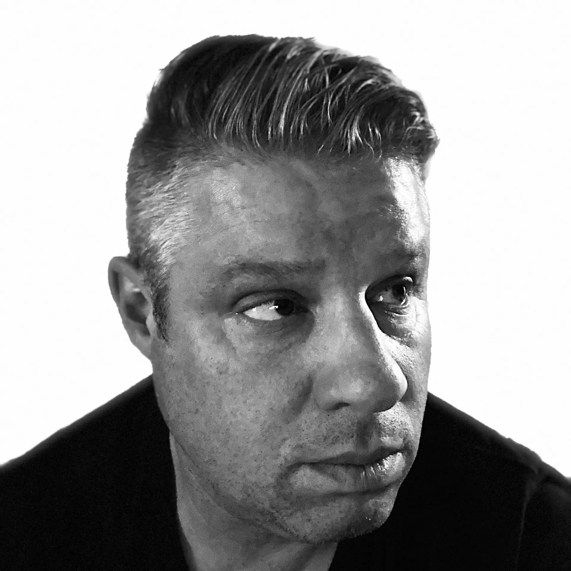 A black and white headshot of Joshua Vermillion, who is wearing a black shirt and looking off to the side