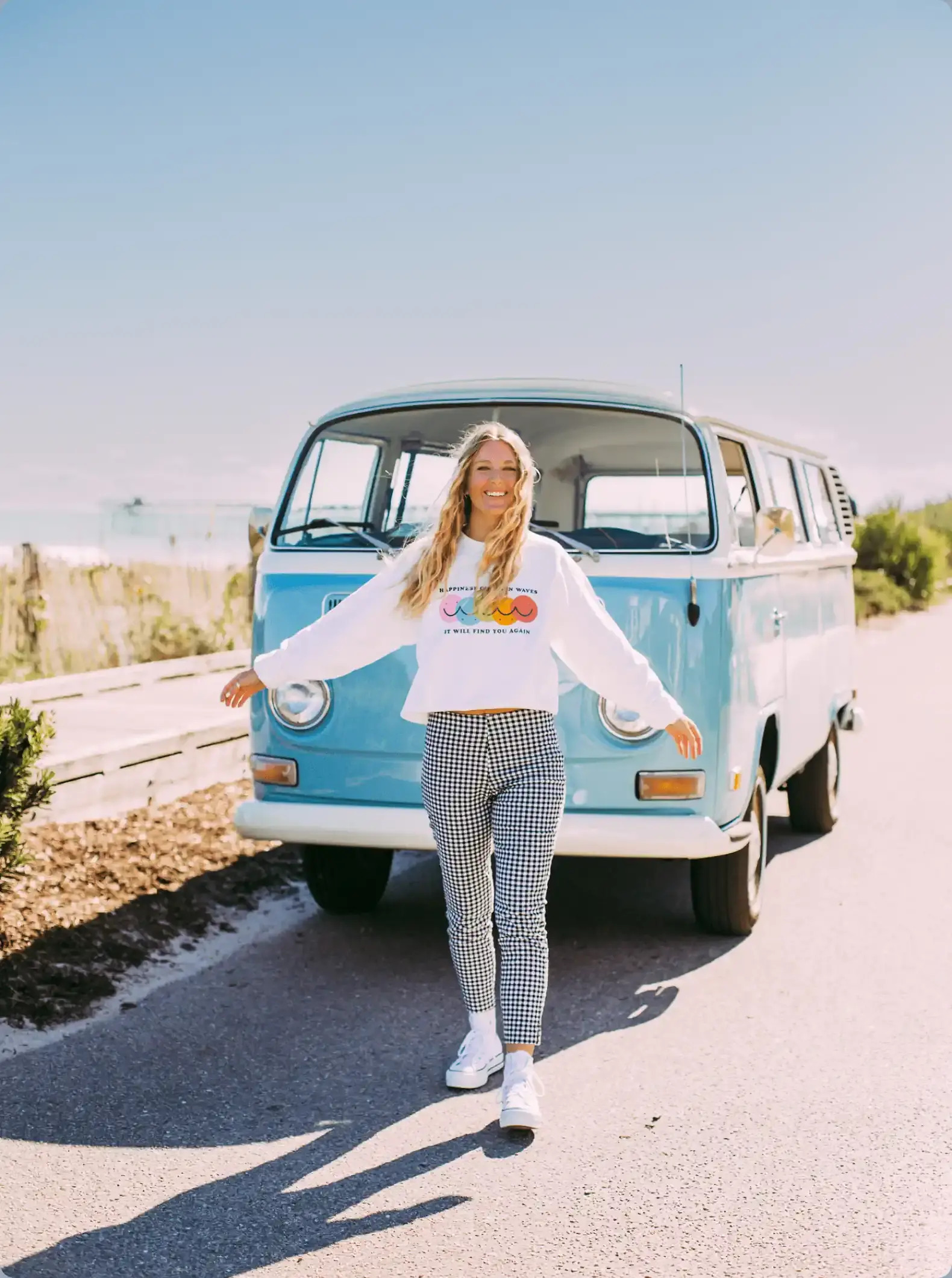 Devin Kane standing in front of a blue Volkswagen bus wearing her custom-designed sweatshirt.