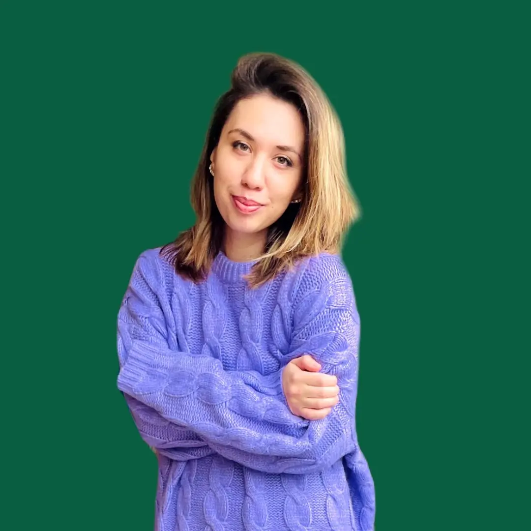 A woman with brown hair smiling at the camera, wearing a purple top against a green background. 