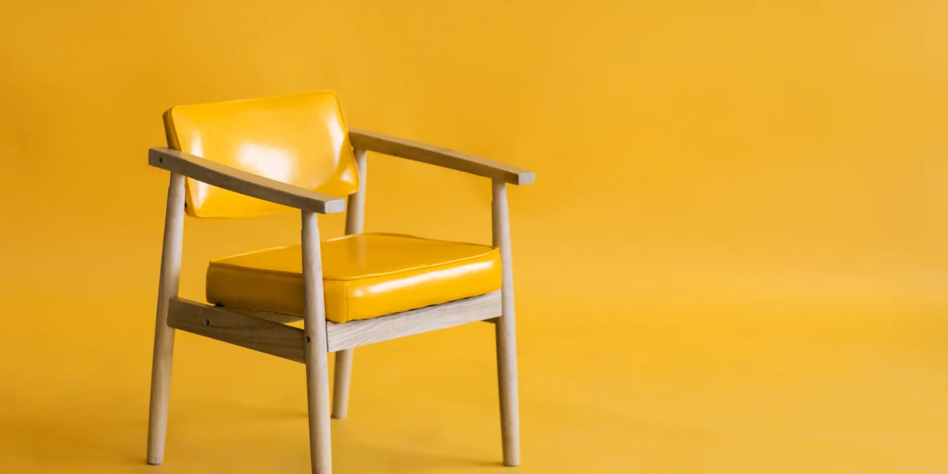A wooden chair with a yellow seat and back sitting on one side of an otherwise empty yellow room.