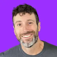 A headshot of Will Draper against a purple background. Will is wearing a gray t-shirt and smiling casually. 